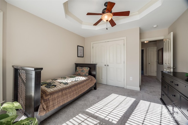 bedroom featuring ceiling fan, light colored carpet, a raised ceiling, and a closet