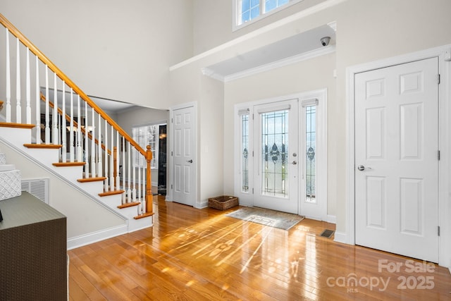 foyer entrance with wood-type flooring, ornamental molding, and a high ceiling