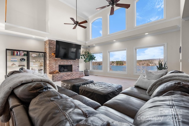 living room featuring ceiling fan, a brick fireplace, a towering ceiling, carpet, and ornamental molding