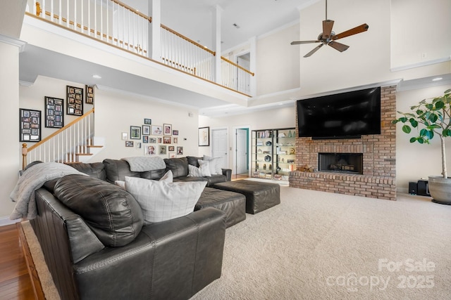 living room with a towering ceiling, a brick fireplace, ceiling fan, and ornamental molding