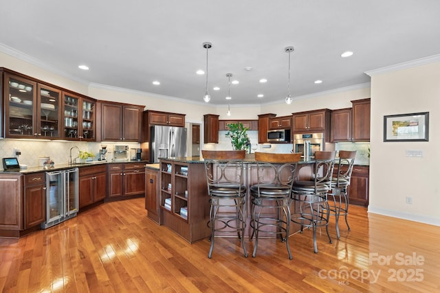 kitchen with appliances with stainless steel finishes, dark stone counters, beverage cooler, pendant lighting, and an island with sink