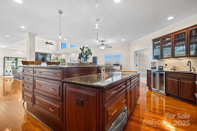 kitchen with sink, beverage cooler, dark stone counters, decorative light fixtures, and a kitchen island with sink