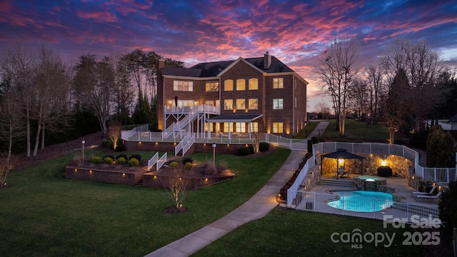 back of property at dusk with a chimney, a deck, a fenced backyard, a yard, and stairs