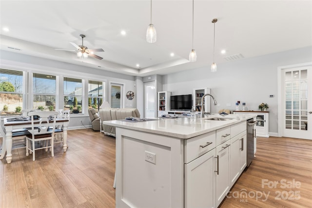 kitchen featuring light stone countertops, hanging light fixtures, a center island with sink, white cabinets, and sink