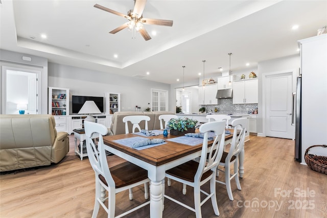 dining area featuring light hardwood / wood-style floors, ceiling fan, and a raised ceiling