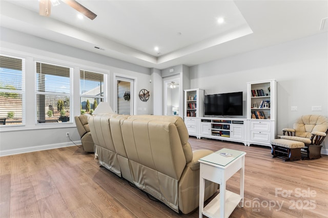 living room with ceiling fan, a tray ceiling, and light hardwood / wood-style floors