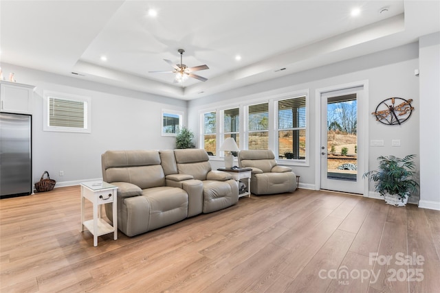 living room with a raised ceiling, ceiling fan, and light hardwood / wood-style flooring