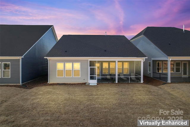 back house at dusk featuring a lawn and a sunroom