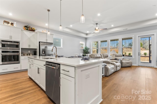 kitchen with a kitchen island with sink, hanging light fixtures, ceiling fan, a tray ceiling, and white cabinets