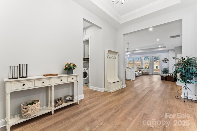 foyer featuring ornamental molding, light hardwood / wood-style flooring, washer / clothes dryer, and a raised ceiling