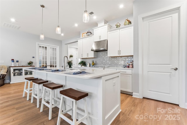 kitchen featuring hanging light fixtures, an island with sink, tasteful backsplash, a breakfast bar area, and white cabinets