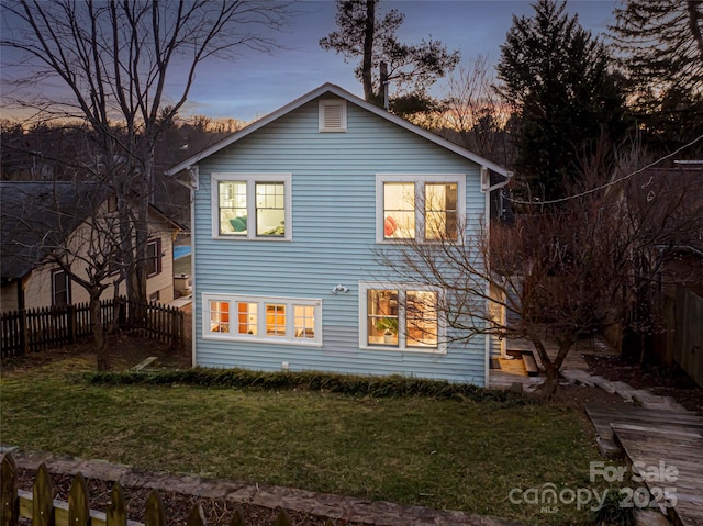 back house at dusk featuring a lawn