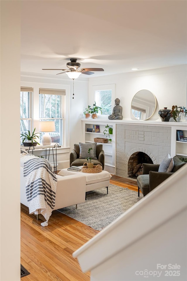 living room with ceiling fan, plenty of natural light, a fireplace, and hardwood / wood-style floors