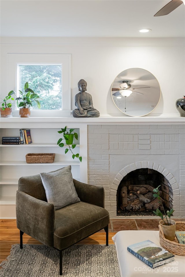 living area featuring ceiling fan, wood-type flooring, and a fireplace