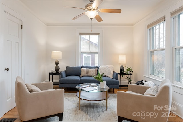 living room featuring light wood-type flooring, ceiling fan, ornamental molding, and a healthy amount of sunlight