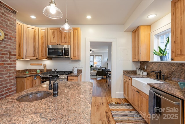 kitchen featuring appliances with stainless steel finishes, sink, dark stone counters, and decorative light fixtures