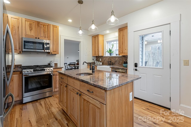 kitchen with an island with sink, appliances with stainless steel finishes, decorative light fixtures, dark stone countertops, and sink