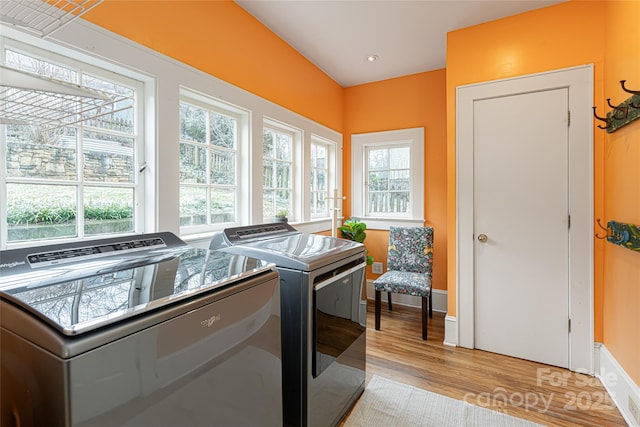 clothes washing area with a wealth of natural light, washer and dryer, and light hardwood / wood-style floors