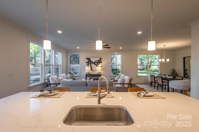 kitchen with light stone counters, plenty of natural light, ceiling fan, sink, and hanging light fixtures