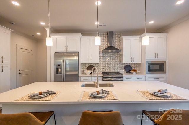 kitchen featuring appliances with stainless steel finishes, sink, wall chimney range hood, decorative light fixtures, and a large island