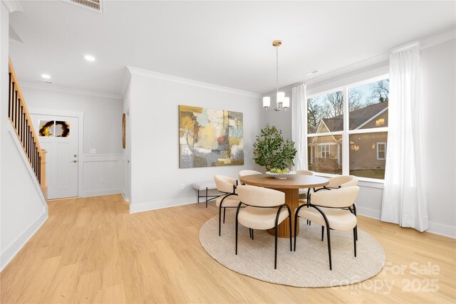 dining space featuring light wood-style floors, crown molding, stairway, and an inviting chandelier