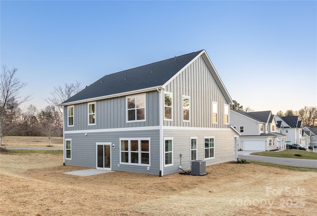 rear view of house with board and batten siding, a shingled roof, and central AC unit