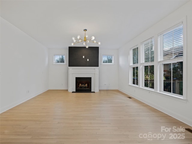 unfurnished living room featuring light hardwood / wood-style floors, a wealth of natural light, and a chandelier