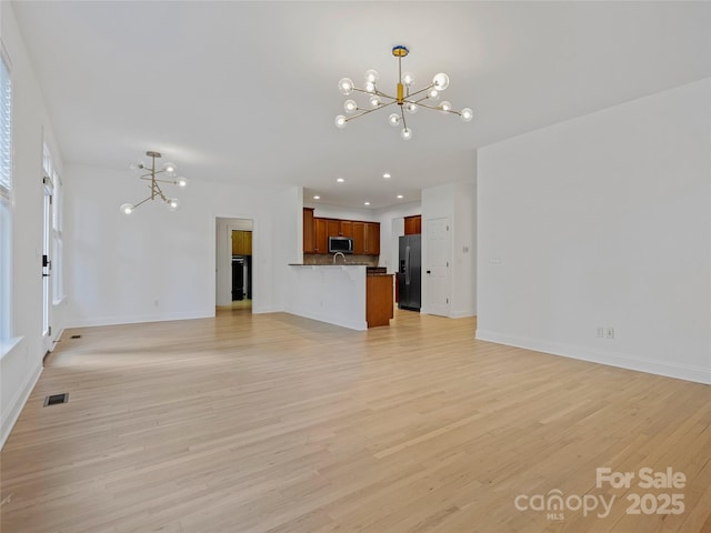 unfurnished living room featuring a notable chandelier and light hardwood / wood-style flooring