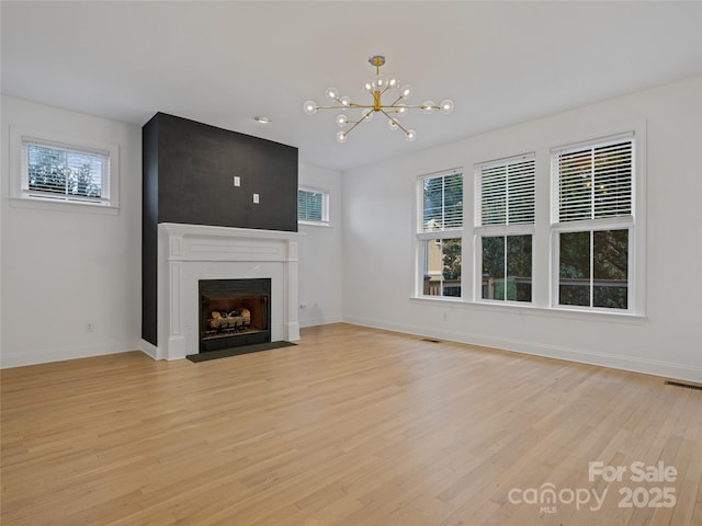 unfurnished living room featuring a high end fireplace, a chandelier, light wood-type flooring, and a wealth of natural light