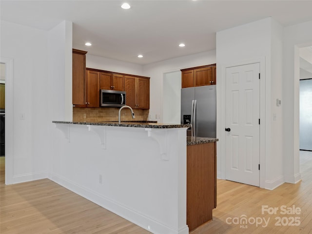 kitchen with kitchen peninsula, decorative backsplash, a kitchen bar, appliances with stainless steel finishes, and dark stone countertops