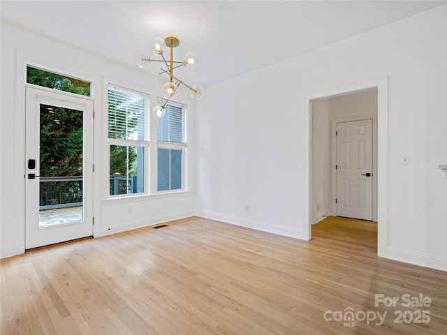 empty room featuring a notable chandelier and light hardwood / wood-style flooring