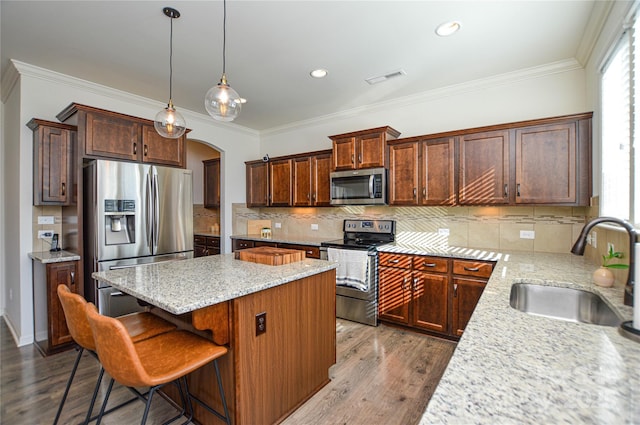 kitchen with sink, light stone countertops, appliances with stainless steel finishes, a kitchen island, and wood-type flooring