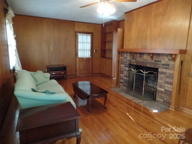 living room featuring a brick fireplace, wood-type flooring, wood walls, and ceiling fan