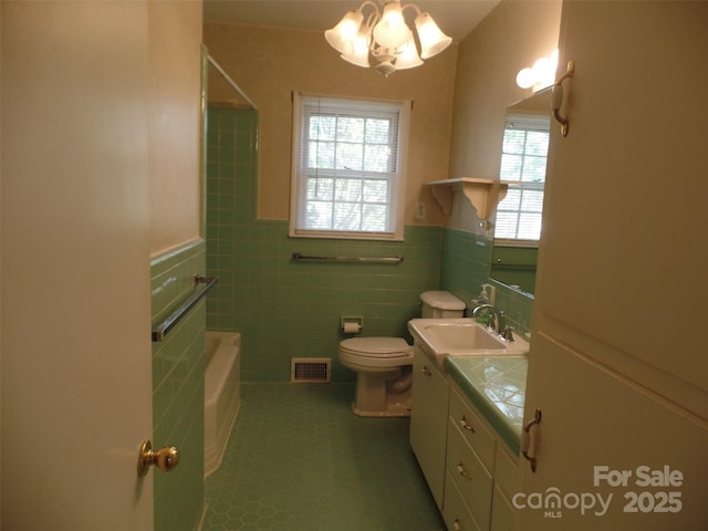 bathroom with toilet, vanity, tile walls, tile patterned floors, and a chandelier