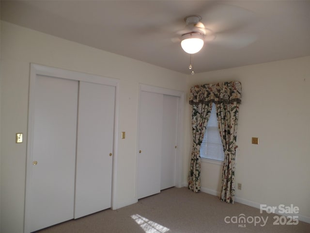 unfurnished bedroom with ceiling fan, multiple closets, and light carpet