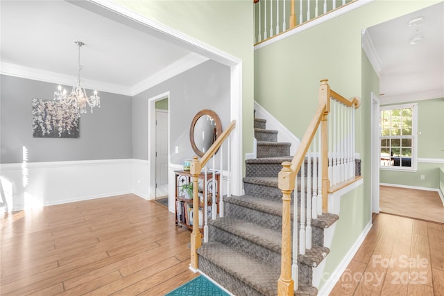 stairs with ornamental molding, wood-type flooring, and a notable chandelier