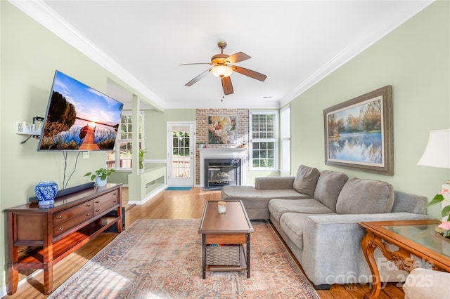 living room featuring a brick fireplace, light hardwood / wood-style flooring, ceiling fan, and crown molding