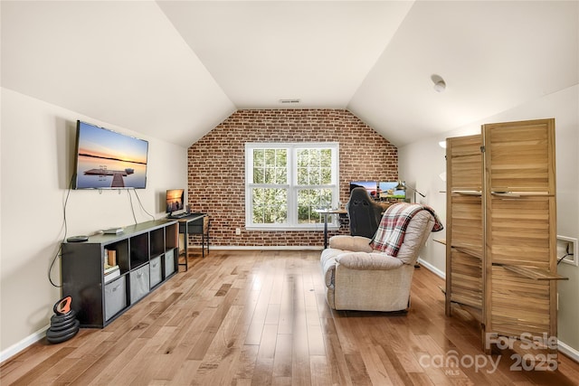 living area featuring wood-type flooring, lofted ceiling, and brick wall