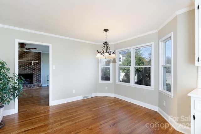 unfurnished dining area with dark hardwood / wood-style floors, crown molding, a fireplace, and ceiling fan with notable chandelier