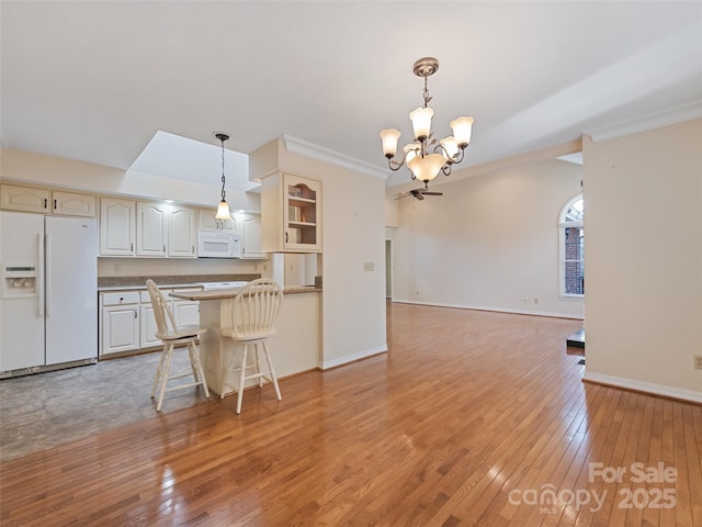 kitchen featuring a kitchen bar, hanging light fixtures, white appliances, and light hardwood / wood-style floors