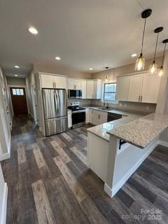 kitchen featuring a breakfast bar, kitchen peninsula, appliances with stainless steel finishes, decorative light fixtures, and white cabinetry