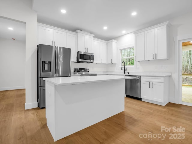 kitchen with appliances with stainless steel finishes, light hardwood / wood-style flooring, white cabinetry, and a kitchen island