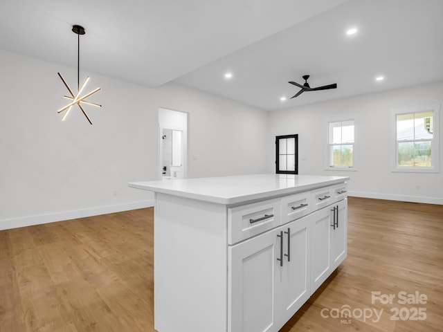 kitchen featuring pendant lighting, a center island, ceiling fan with notable chandelier, light hardwood / wood-style flooring, and white cabinetry