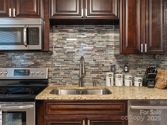 kitchen featuring light stone countertops, backsplash, dark brown cabinets, stainless steel appliances, and sink