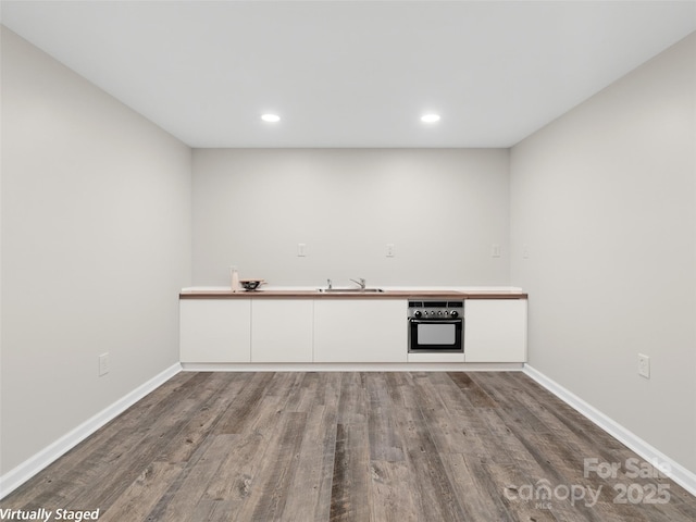 interior space with wall oven, sink, white cabinets, and hardwood / wood-style flooring