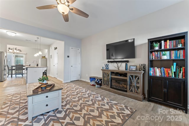 living room with light hardwood / wood-style flooring, ceiling fan with notable chandelier, and sink