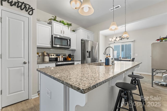 kitchen featuring sink, light stone counters, pendant lighting, a kitchen island with sink, and appliances with stainless steel finishes