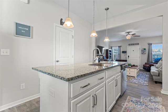 kitchen with sink, ceiling fan, light stone countertops, an island with sink, and wood-type flooring