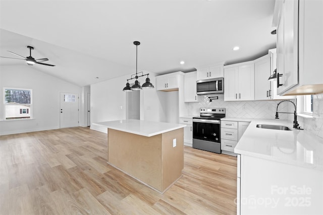 kitchen featuring light wood finished floors, appliances with stainless steel finishes, open floor plan, light countertops, and a sink