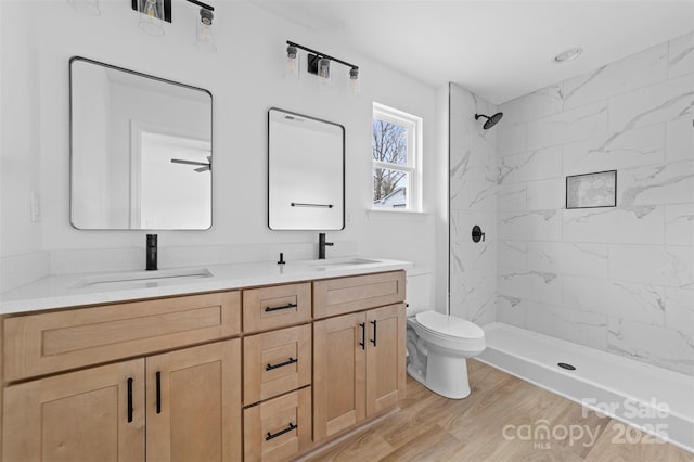 full bath featuring double vanity, a marble finish shower, a sink, and wood finished floors